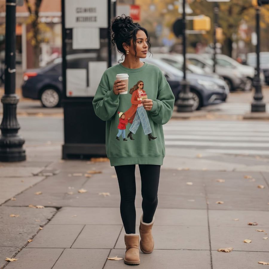 Woman wearing the Wrapped & Running™ sweatshirt by Blossombless.co in Light Green with black leggings and tan boots, holding a coffee on a city sidewalk