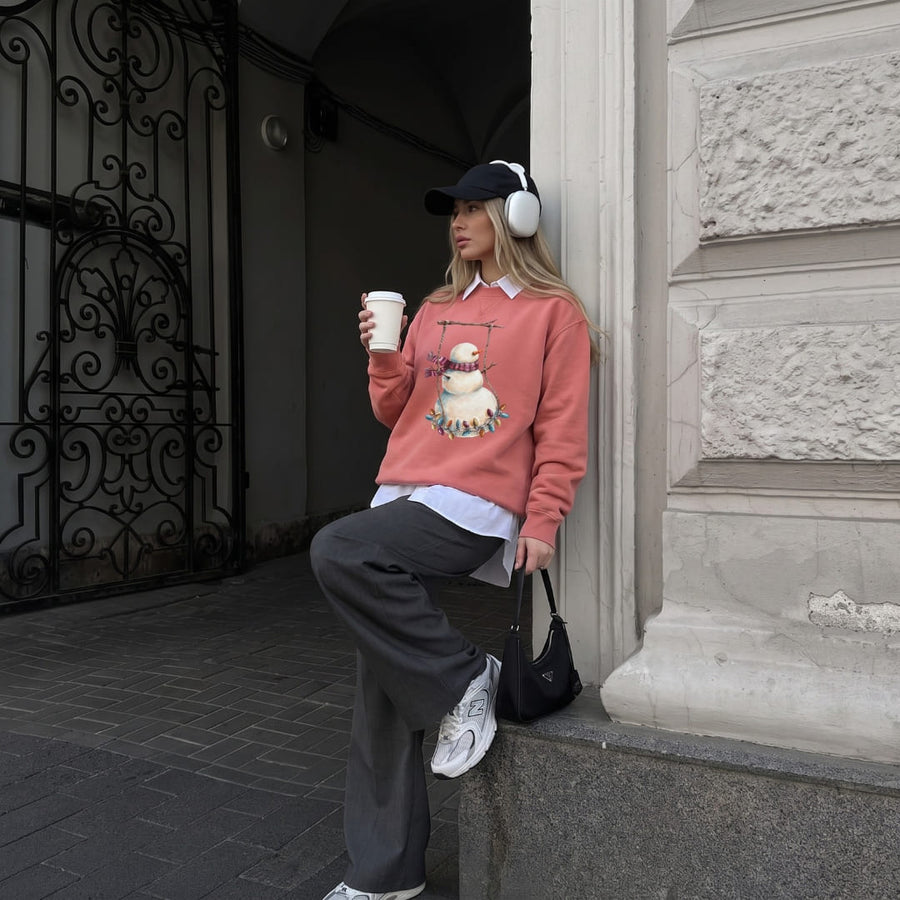 Woman wearing the Swing Season™ sweatshirt by Blossombless.co in Crimson with black trousers, white sneakers and headphones, leaning in a stone doorway with a coffee