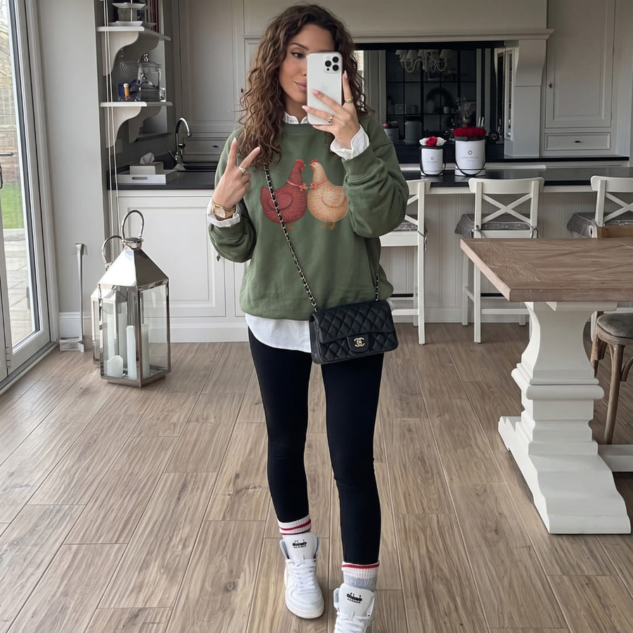 Woman wearing the Belle & Plume™ sweatshirt by Blossombless.co in Blue Spruce with black leggings, white sneakers and a black quilted crossbody bag, taking a mirror selfie in a bright kitchen