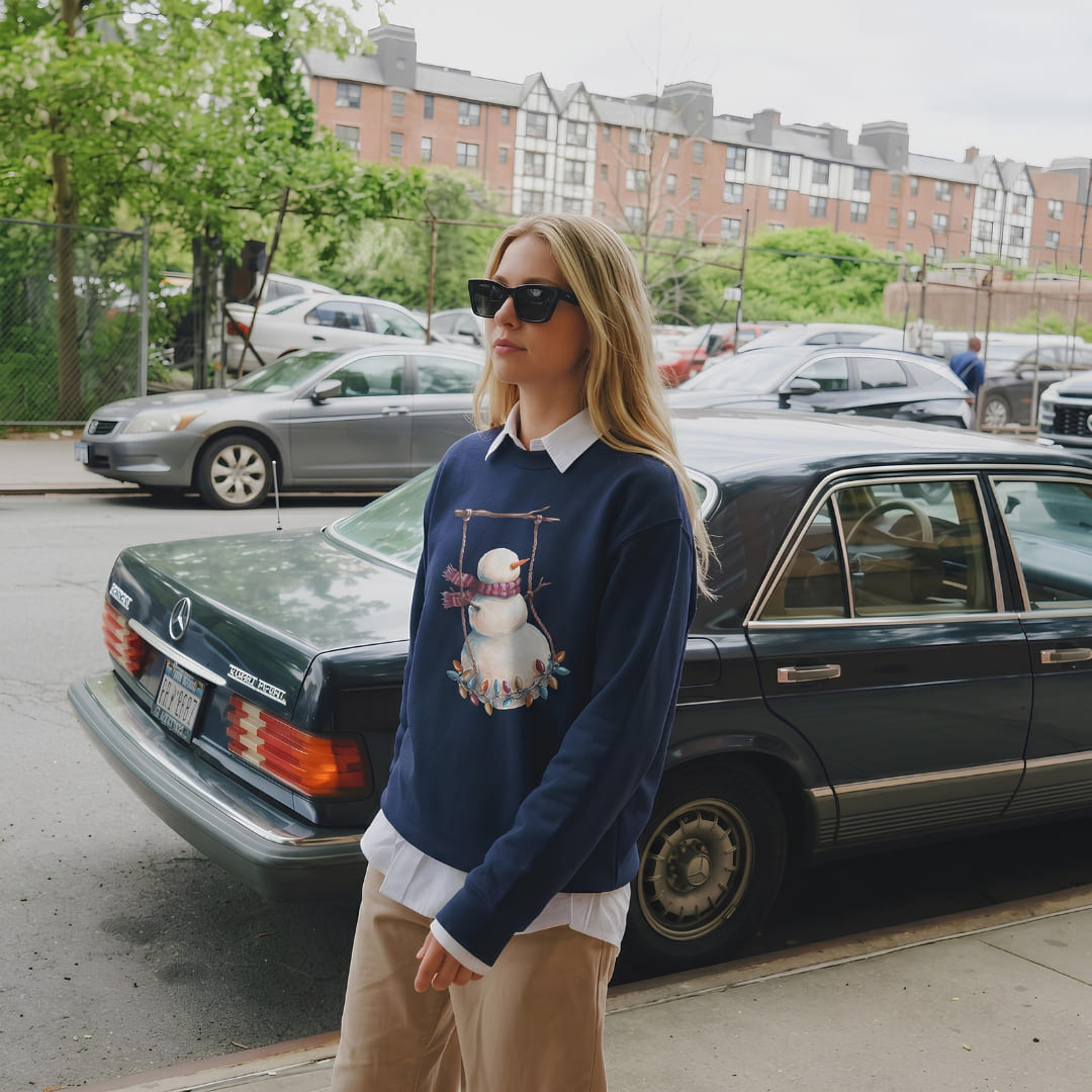 Woman wearing the Swing Season™ sweatshirt by Blossombless.co in True Navy over a white collared shirt with tan trousers and sunglasses, standing beside a vintage black car