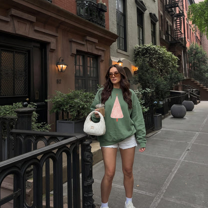 Woman wearing the Pink Pine™ sweatshirt by Blossombless.co in Light Green with shorts and a small white bag, walking past brownstones