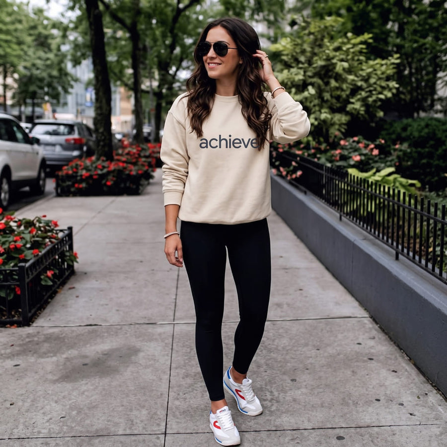 Achieve™ oversized sweatshirt by Blossombless.co in Dust, lifestyle: woman in black leggings and sunglasses on a tree-lined city sidewalk