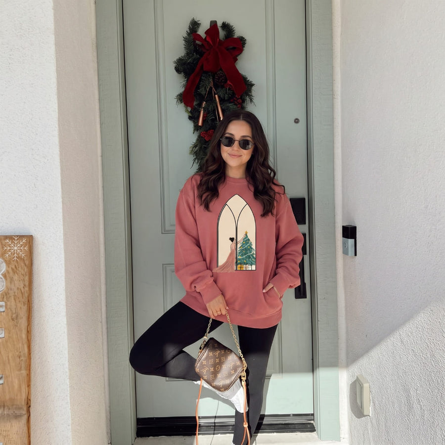 Woman in sunglasses wearing the Star of the Season™ sweatshirt by Blossombless.co in Crimson with black leggings, posing by a green front door with a holiday wreath