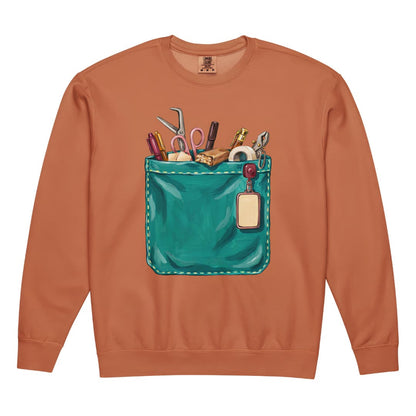 The Shift Pocket™ nurse sweatshirt in Yam, front view: hand-painted teal scrub pocket holding trauma shears, a hemostat, pens, tape and a badge reel