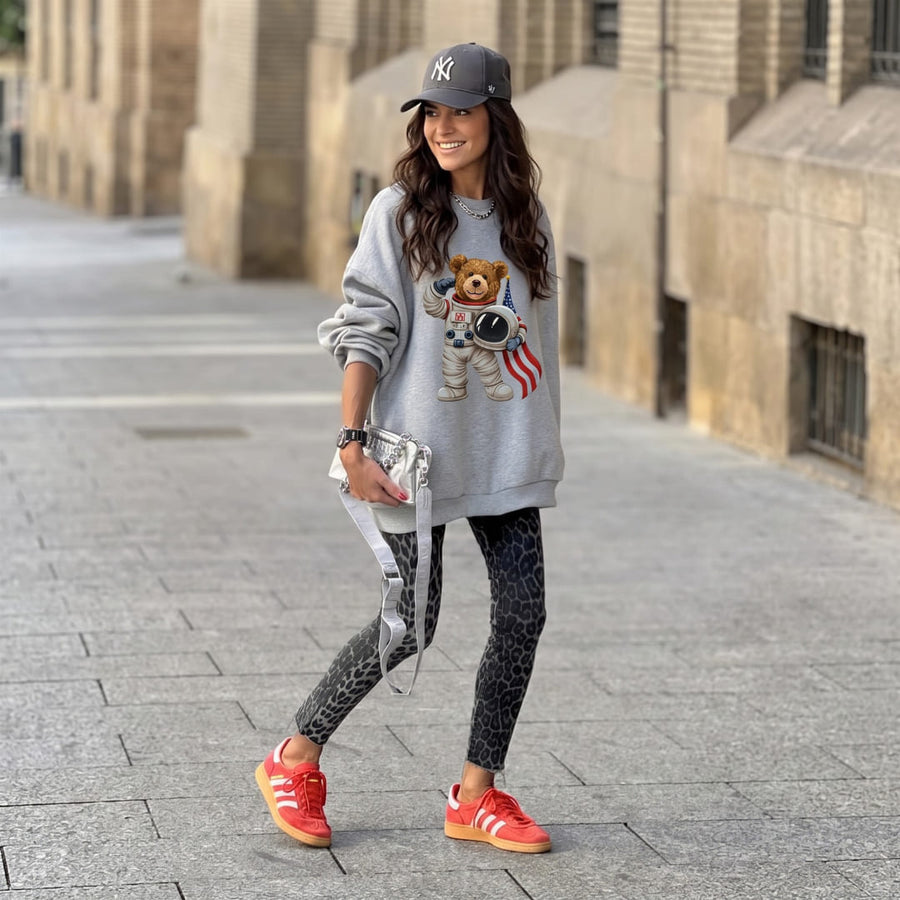 Captain Astro Teddy™ oversized sweatshirt by Blossombless.co in Athletic Heather, lifestyle: woman in black leggings, a cap and red sneakers walking down a stone street