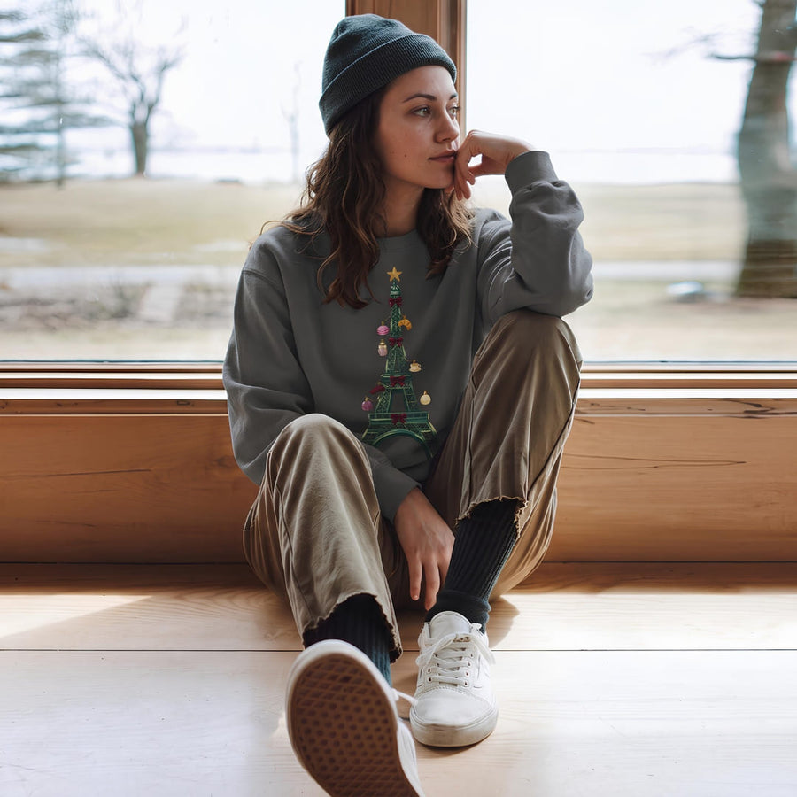 Woman in the Tour de Noël™ Eiffel Tower Christmas sweatshirt in Pepper, sitting by a window in a beanie and cords