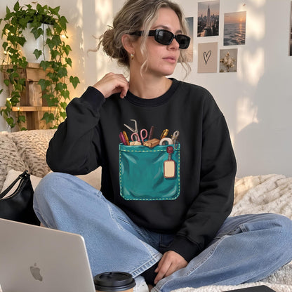 Woman wearing The Shift Pocket™ sweatshirt in Black, sitting on the floor with a laptop and wide-leg jeans
