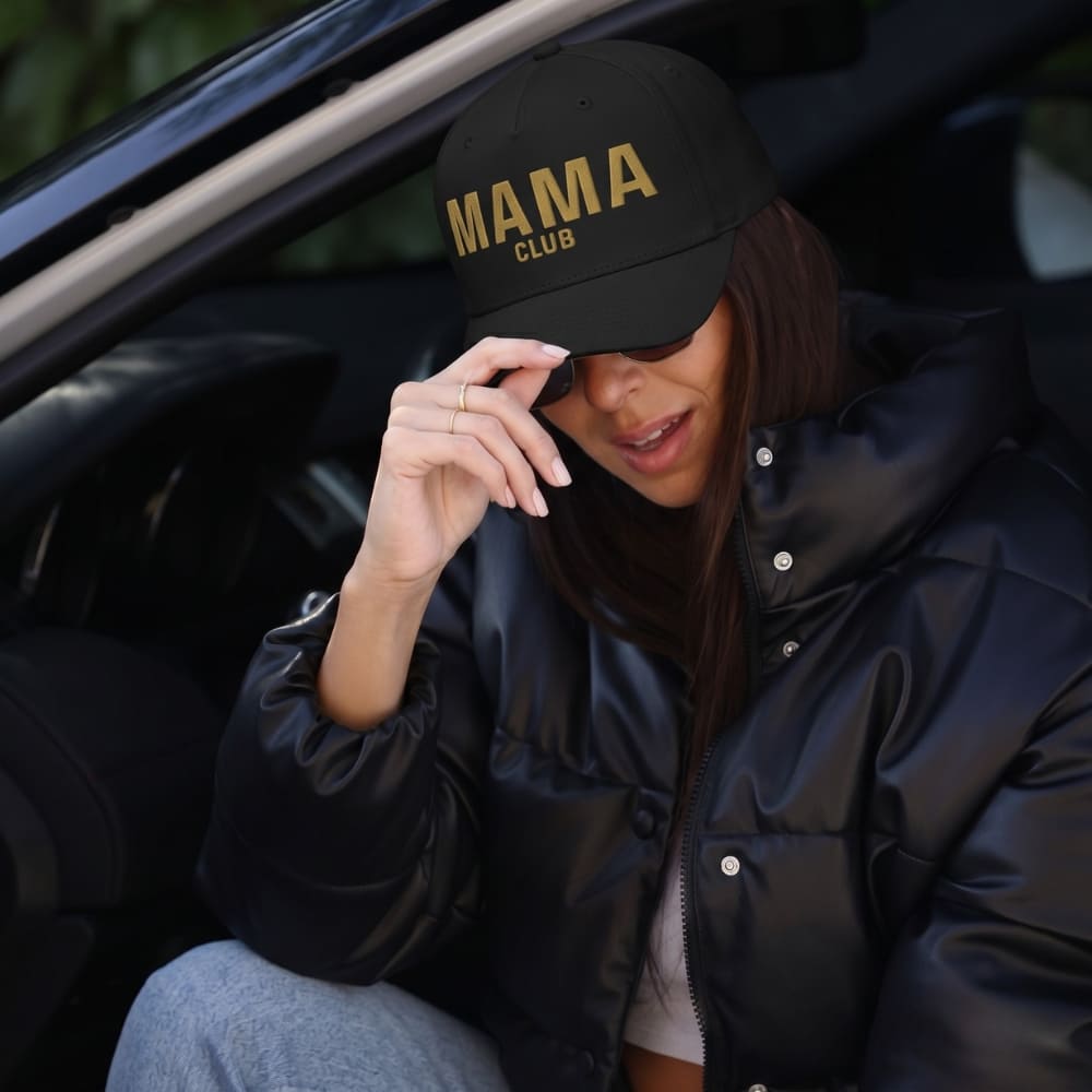 Person wearing a black cap with 'MAMA CLUB' text, sitting inside a vehicle.