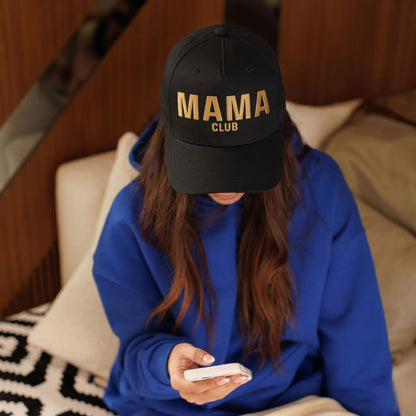 Person wearing a black cap with 'MAMA CLUB' text, sitting on a couch using a phone.