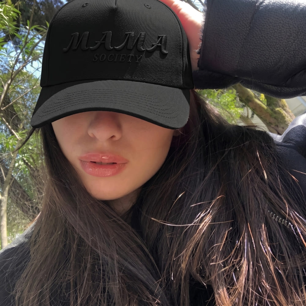 Woman wearing a black cap with 'MAMA SOCIETY' text outdoors