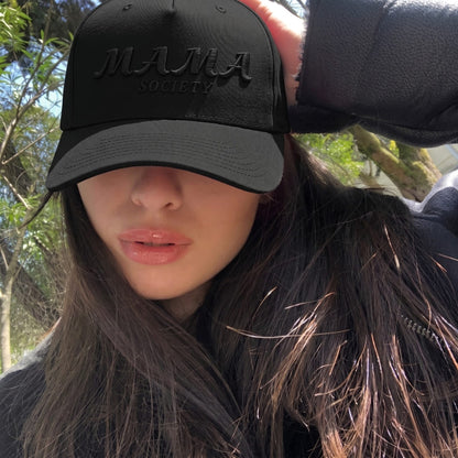 Woman wearing a black cap with 'MAMA SOCIETY' text outdoors