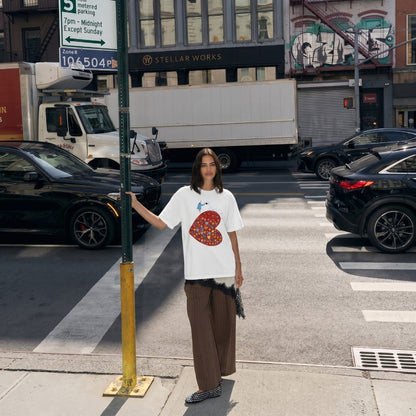 Person wearing a white t-shirt with a colorful heart design on a city street.