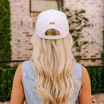 Person wearing a white cap with gold logo outdoors