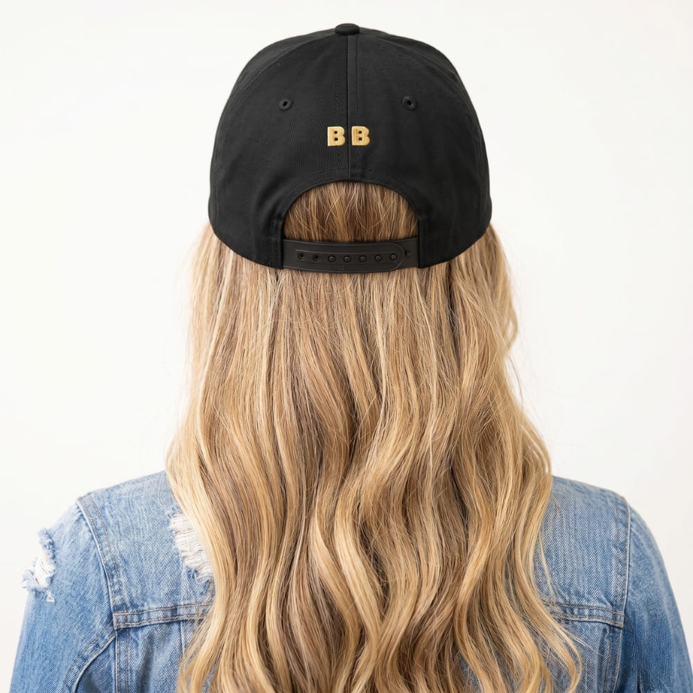 Person wearing a black cap with 'BB' logo and long blonde hair, against a white background