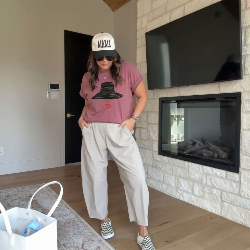 Woman wearing a pink t-shirt with a graphic design and a cap, standing in a living room.