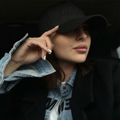 Woman wearing a black cap with 'MAMA SOCIETY' branding, posing against a dark background.