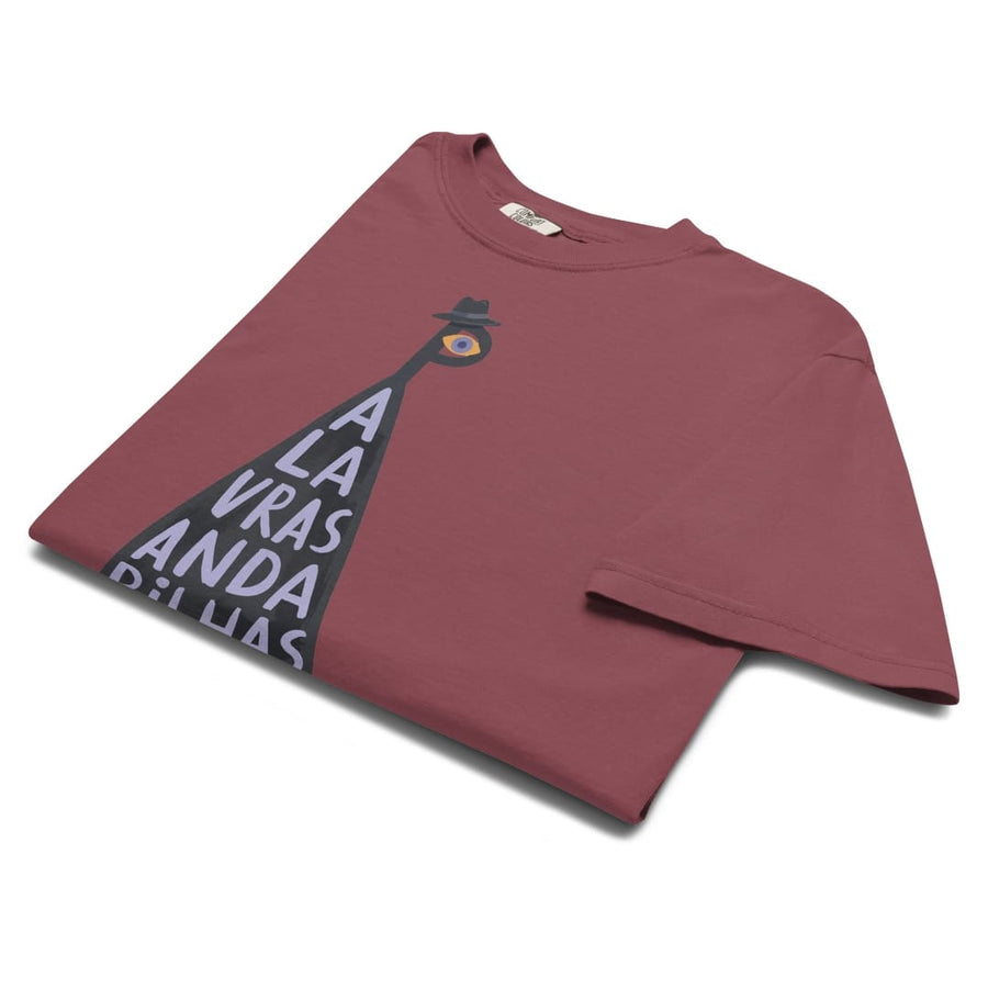 A folded maroon short-sleeve t-shirt with a graphic of a black pyramid sign spelling 'LA VRAZ ANDA DE LLAS' topped with a small figure wearing a hat and a yellow circle, on a white background.