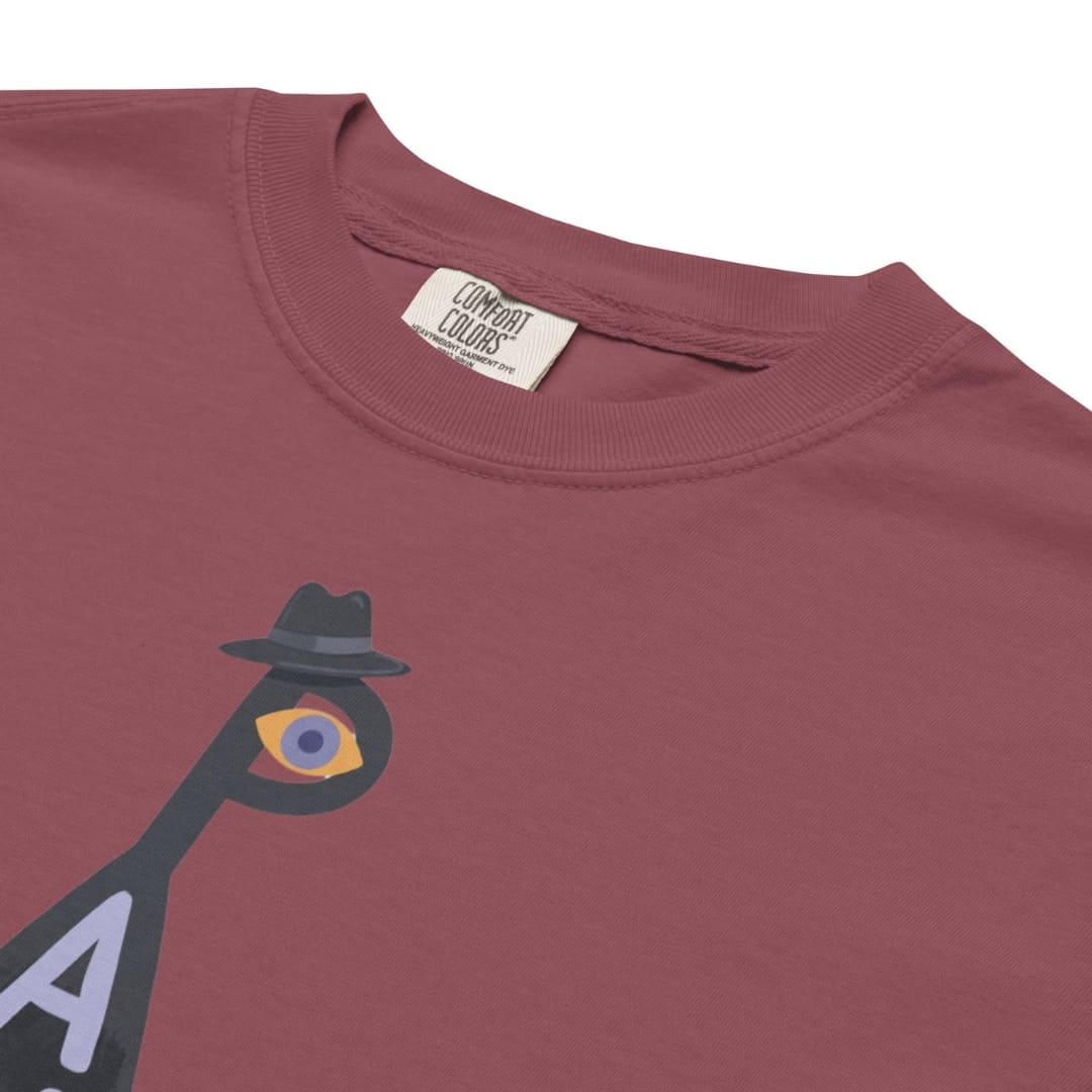 Close-up of a dusty rose crewneck t-shirt featuring a graphic of a bird with a fedora and a single eye, with a visible 'Combat Colors' neck label.