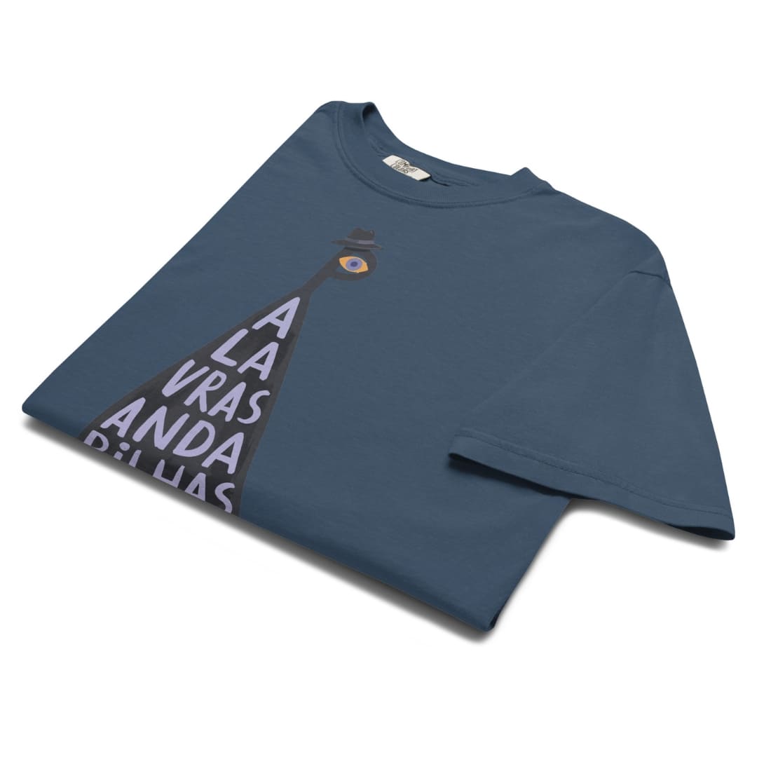 A folded slate blue t-shirt with a graphic print of a lighthouse and the text 'A LA VRAS Y A LA ANDA DE LLAVAS' in white, set against a plain white background.