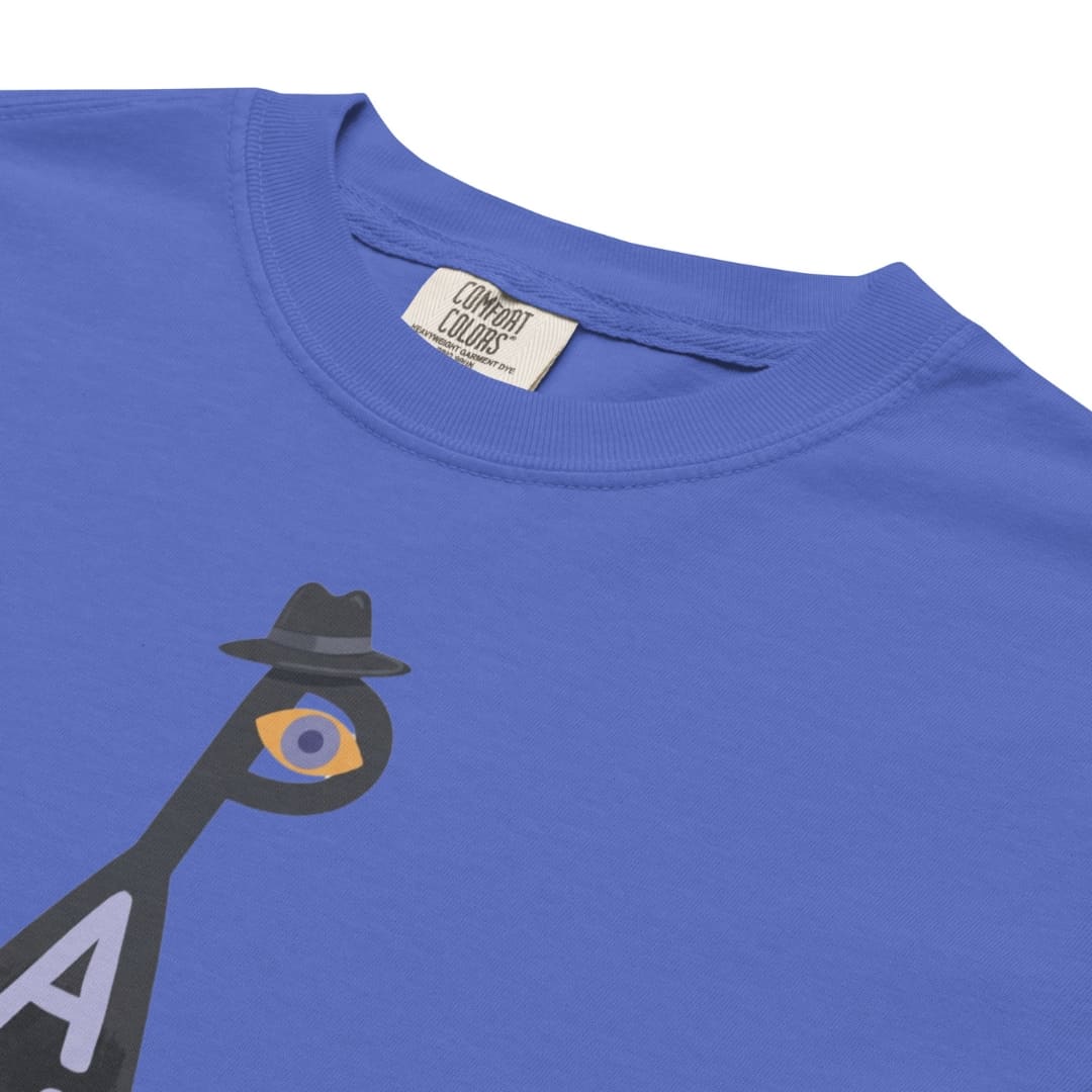 Close-up of a royal blue crewneck t-shirt featuring a graphic of a black silhouette figure wearing a fedora and an eye motif. The inside collar shows a white tag with the brand 'Combat Colors'.