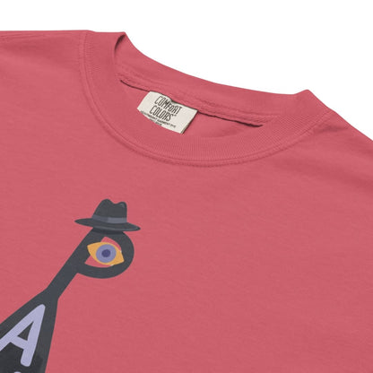 A close-up of a coral pink t-shirt featuring a graphic of a stylized figure with a black hat and a multicolored eye, with a visible 'Combat Colors' neck label.
