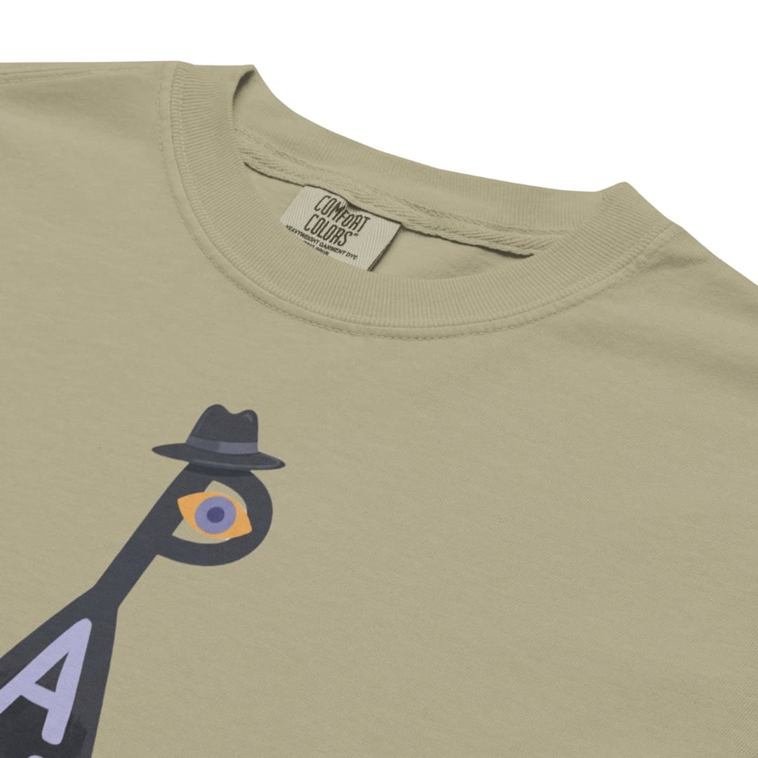 Close-up of a light khaki crewneck t-shirt featuring a graphic of a bird character wearing a black fedora and a purple eye patch. The brand label 'Combat Colors' is visible inside the collar.