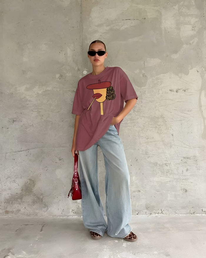 Model in a rust-toned oversized graphic tee, styled with wide-leg denim and a red handbag