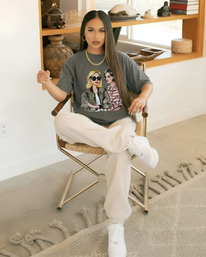 Model seated on a director’s chair wearing an olive graphic tee and cream wide-leg pants