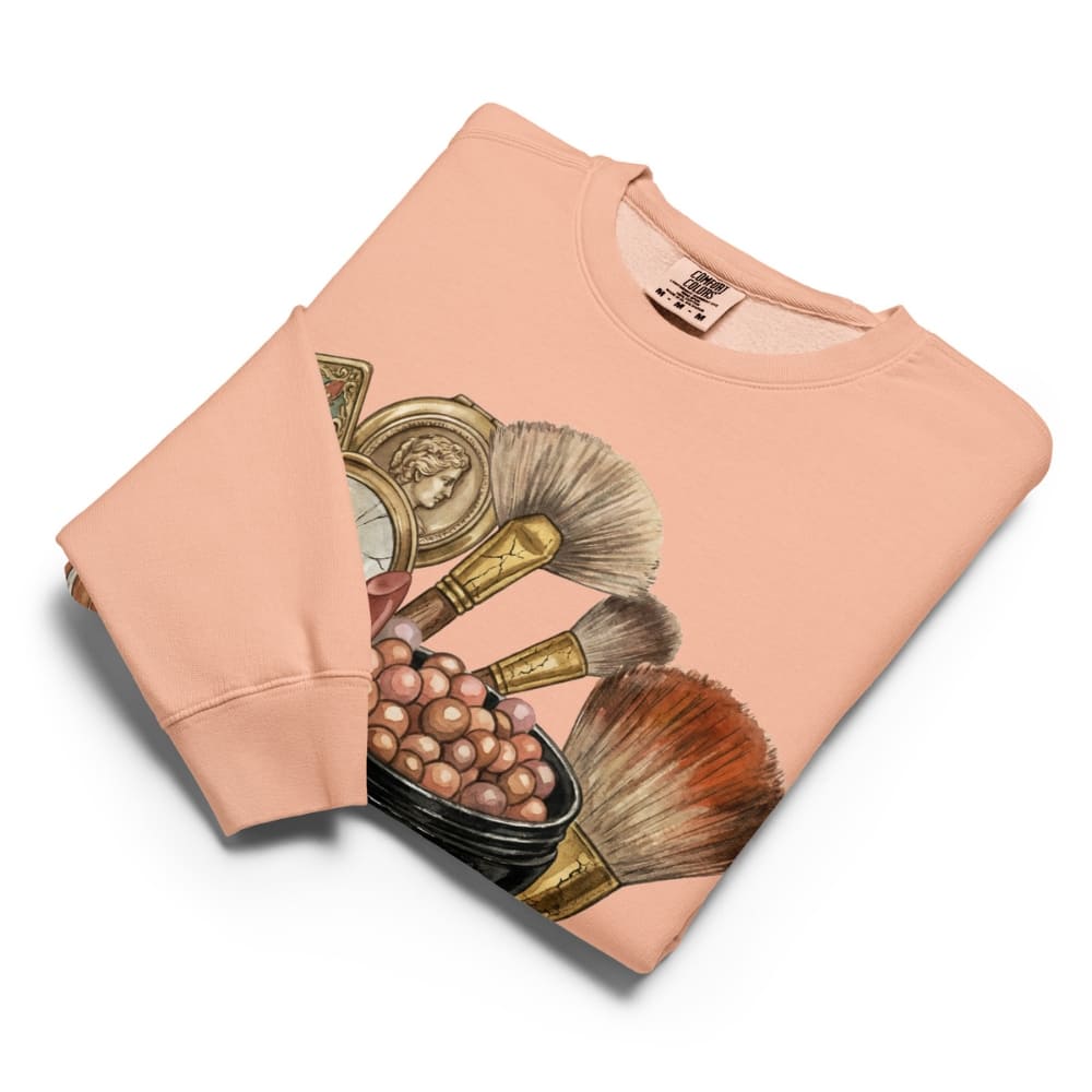 Folded peach-colored sweatshirt with makeup brush design on a white background