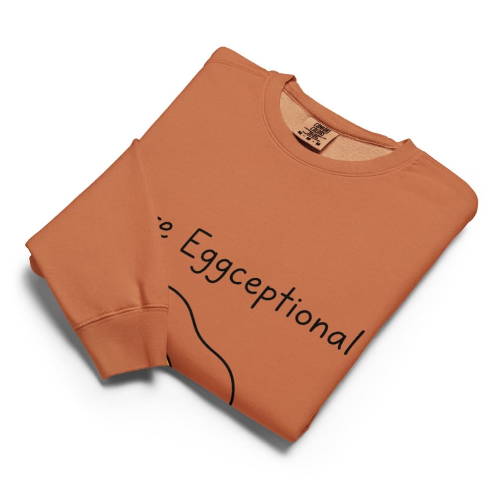 Folded orange sweatshirt with 'Eggceptional' text on a white background