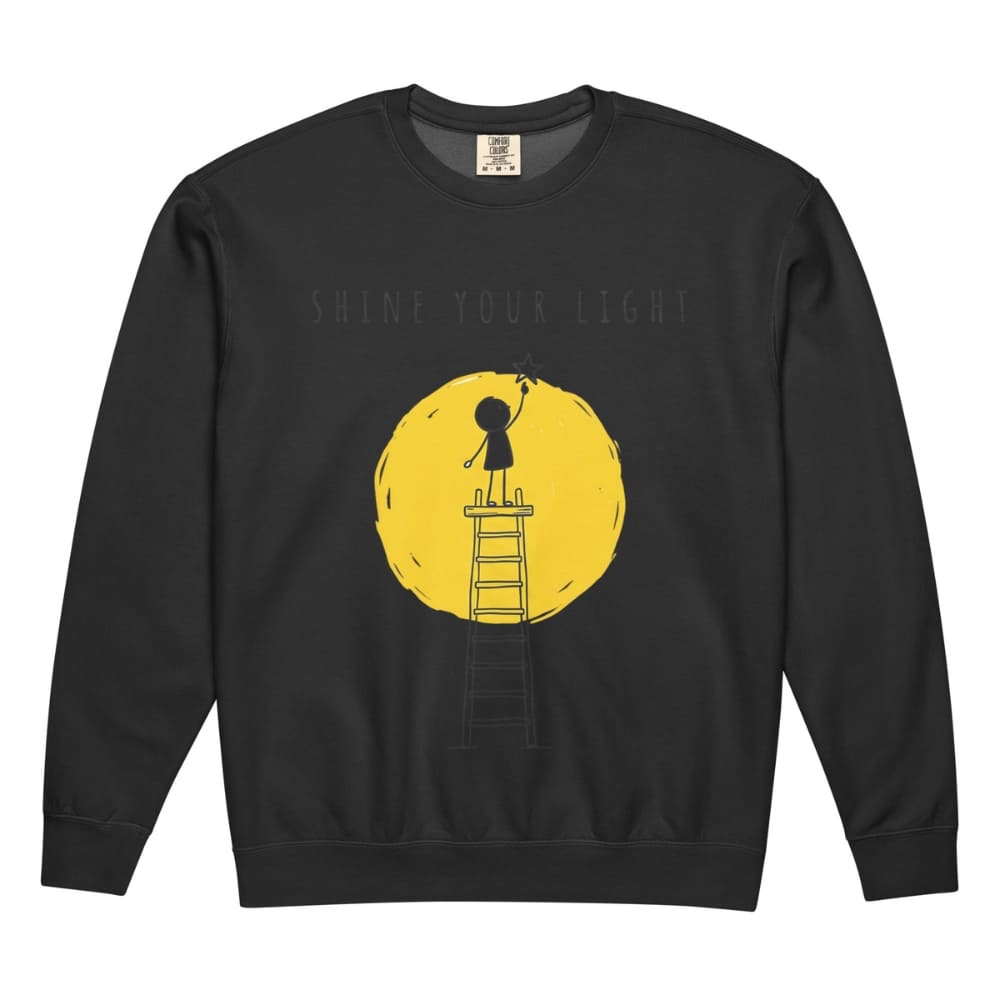 Black sweatshirt with a yellow graphic of a person on a ladder reaching for the text 'Shine Your Light' on a white background.