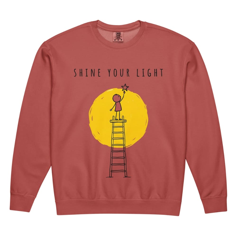Red sweatshirt with a graphic of a person on a ladder reaching for a star, set against a yellow circle with 'Shine Your Light' text.