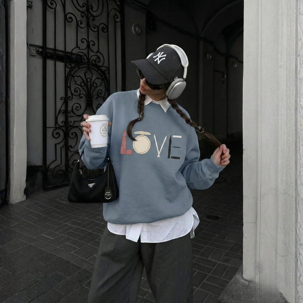 Person wearing a blue sweatshirt with 'LOVE' printed on it, holding a coffee cup, and wearing headphones.