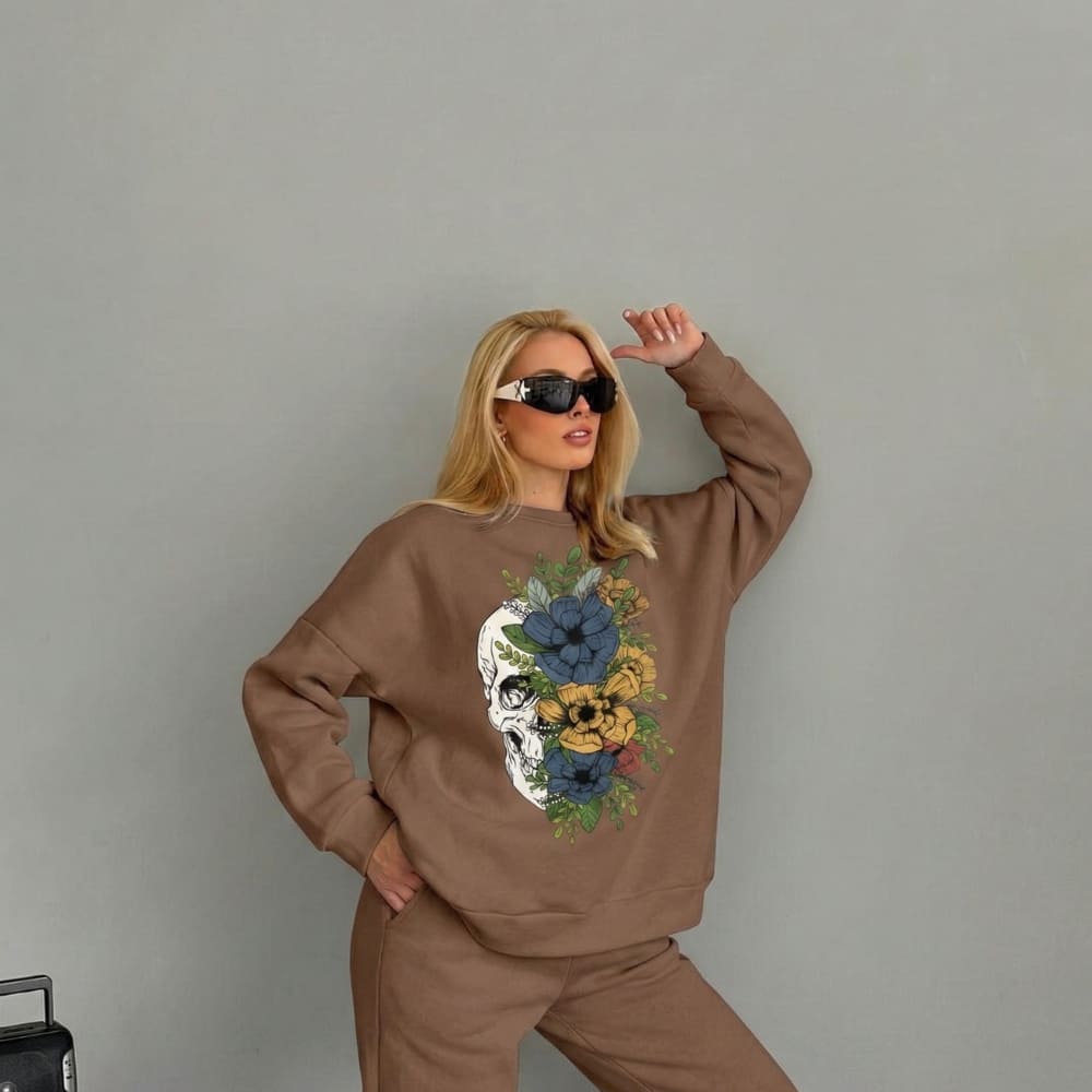 Woman wearing a brown sweatshirt with a skull and floral design against a gray background