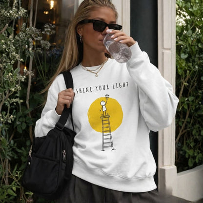 Woman wearing a white sweatshirt with a graphic design and text, drinking from a water bottle outdoors.