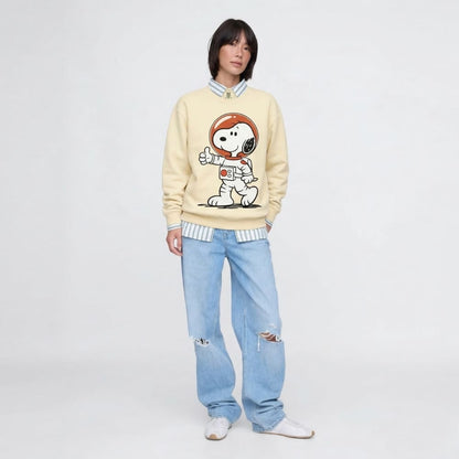 Person wearing a beige sweatshirt with a cartoon character design and light blue jeans on a white background