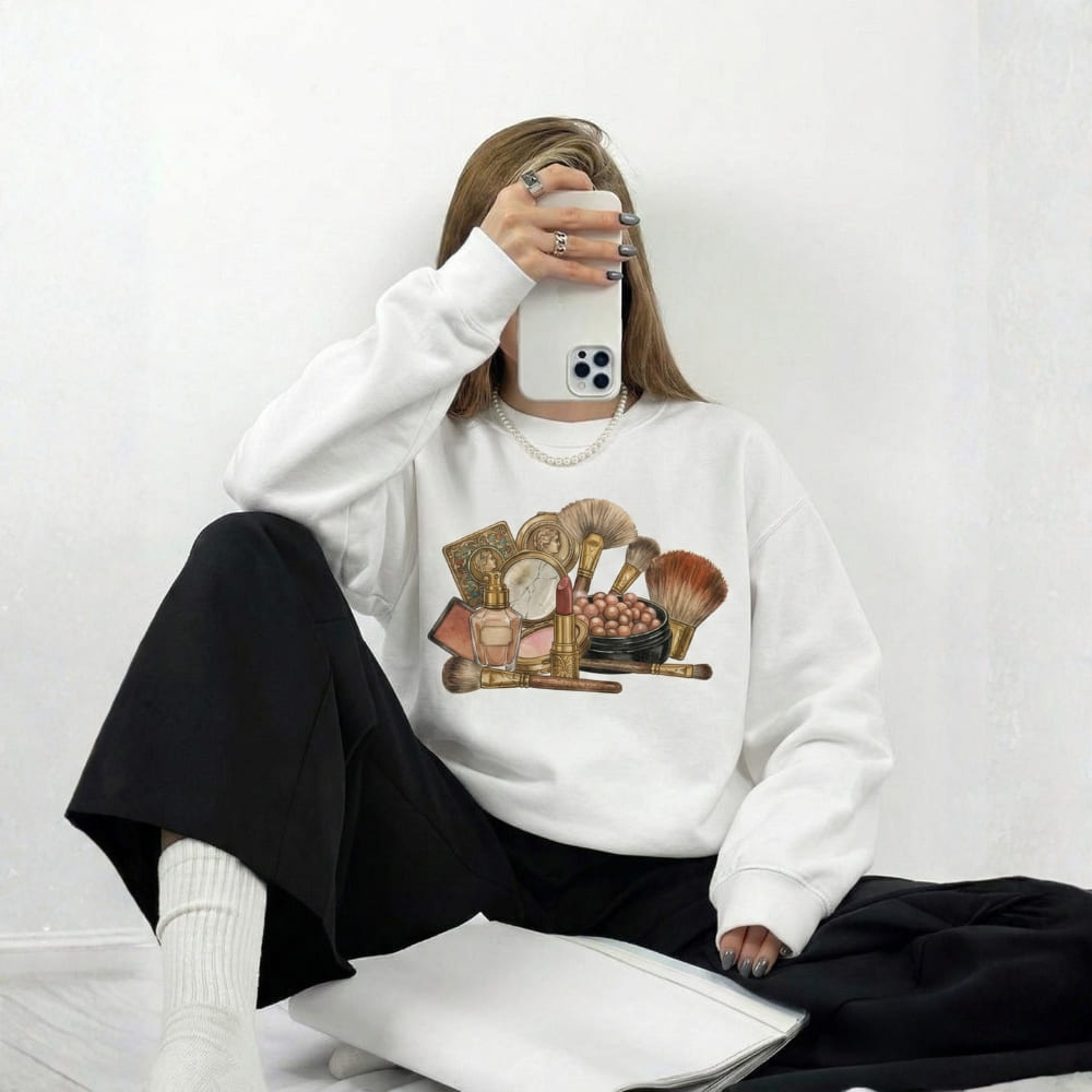 Person wearing a white sweatshirt with makeup graphic, sitting on a white floor.