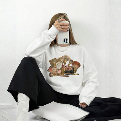 Person wearing a white sweatshirt with makeup graphic, sitting on a white floor.