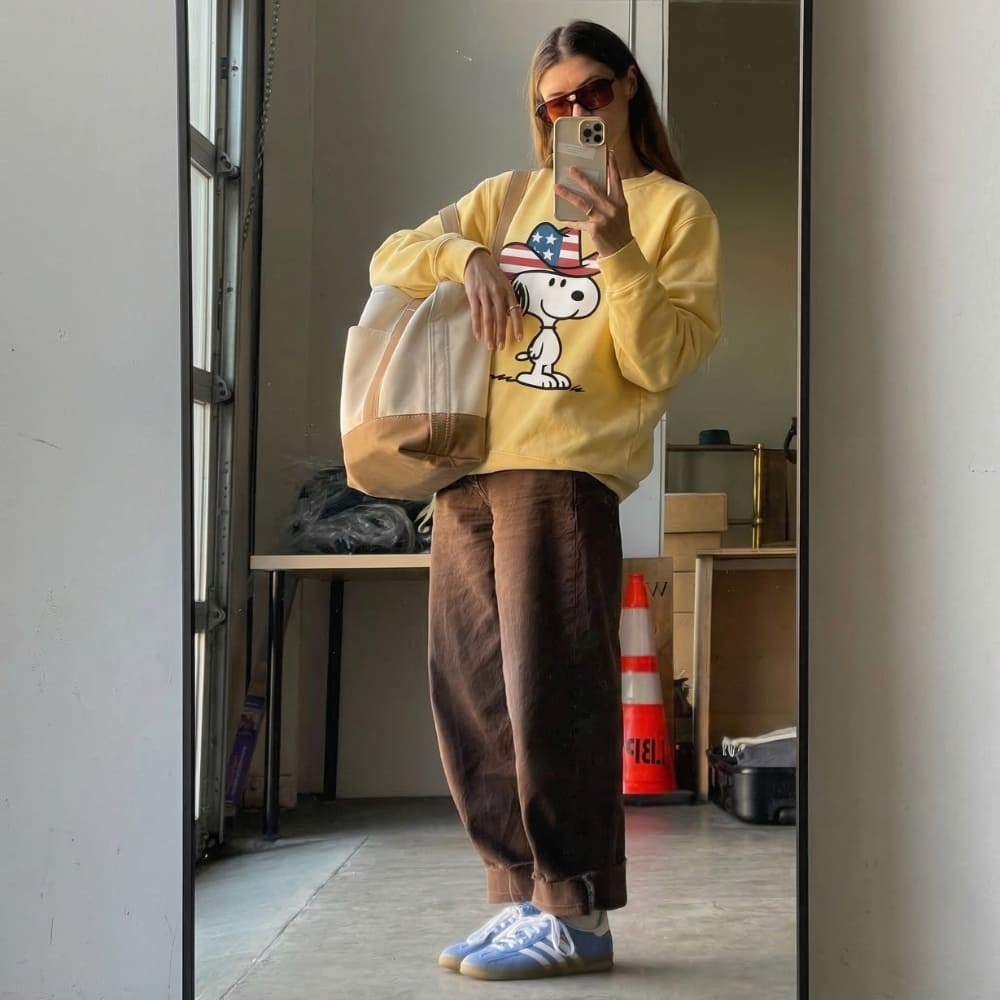 Person wearing a yellow sweatshirt with a graphic design, taking a mirror selfie in an indoor setting.