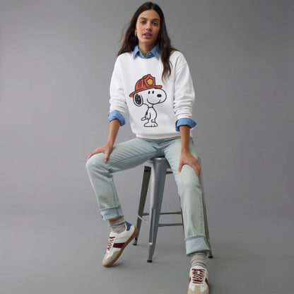 Person wearing a white sweatshirt with a cartoon character, sitting on a stool against a gray background