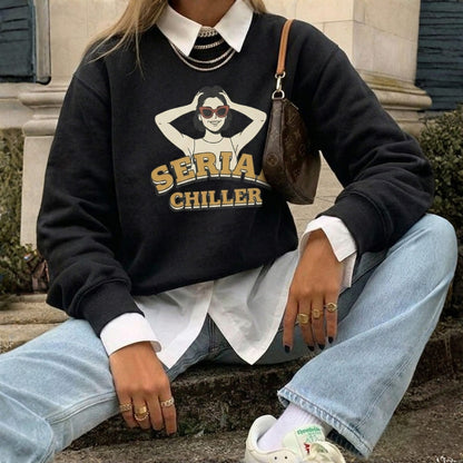 Person wearing a black sweatshirt with graphic design and text, sitting outdoors.