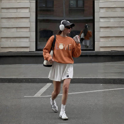 Person wearing an orange sweatshirt with 'LOVE' print, white shorts, and white sneakers on a street.