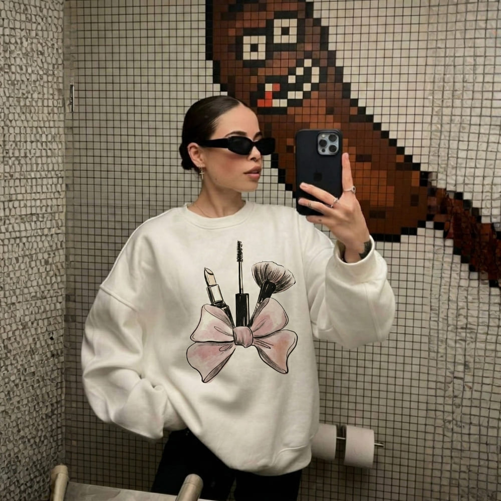 Person wearing a white sweatshirt with makeup graphic in a bathroom setting