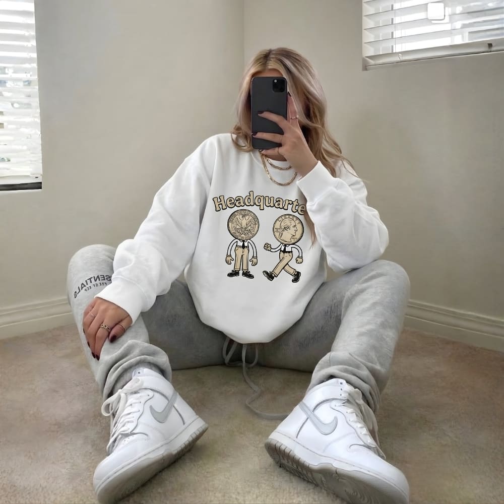 Person wearing a white sweatshirt with graphics and text, sitting on the floor.