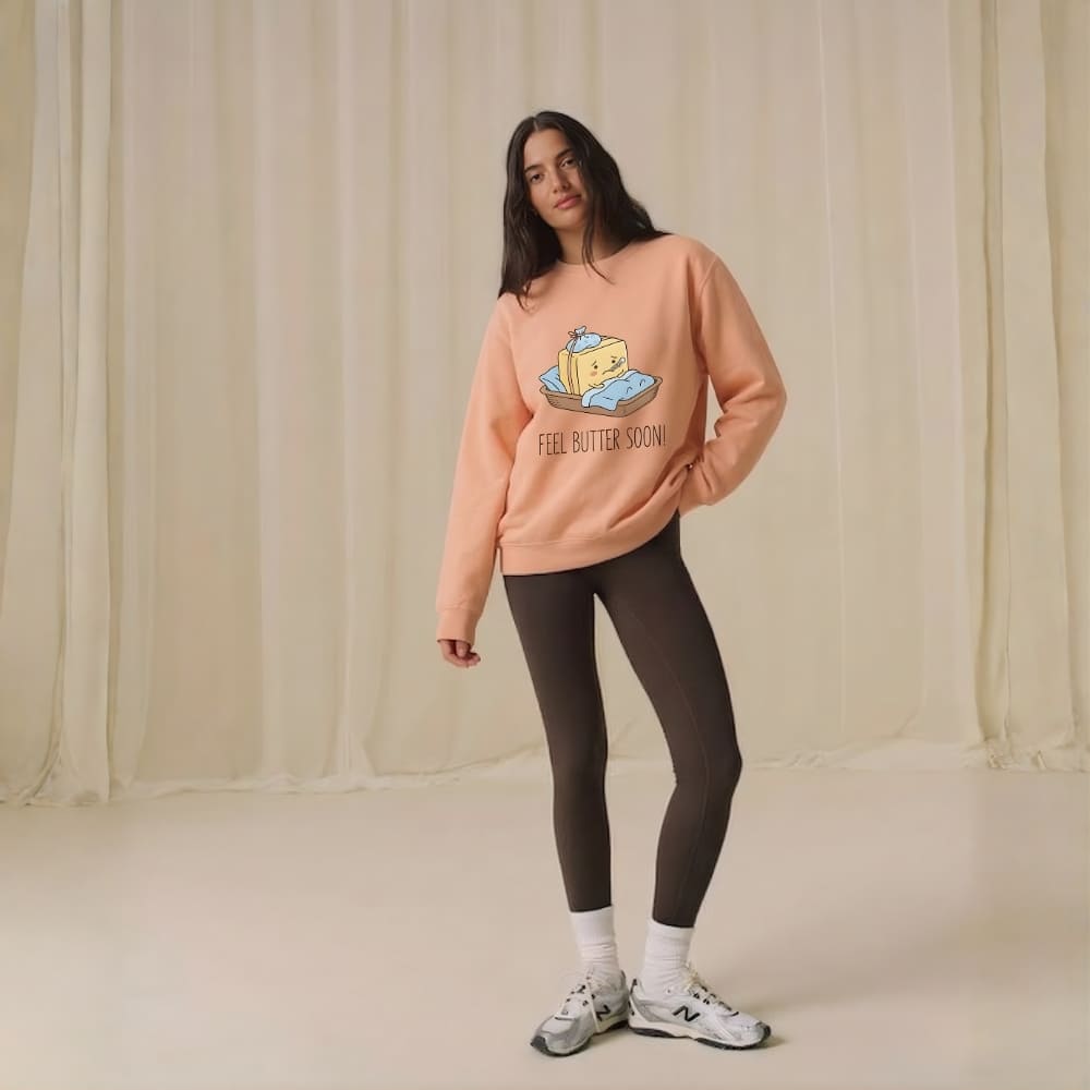Person wearing a peach-colored sweatshirt with a graphic design and text, standing against a plain background