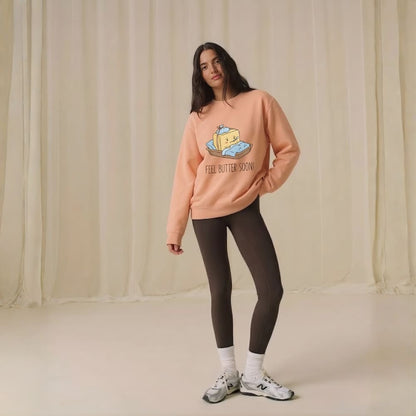 Person wearing a peach-colored sweatshirt with a graphic design and text, standing against a plain background