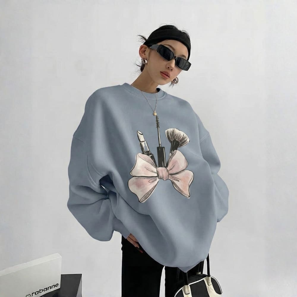 Person wearing a light blue sweatshirt with makeup brush and lipstick design on a plain background