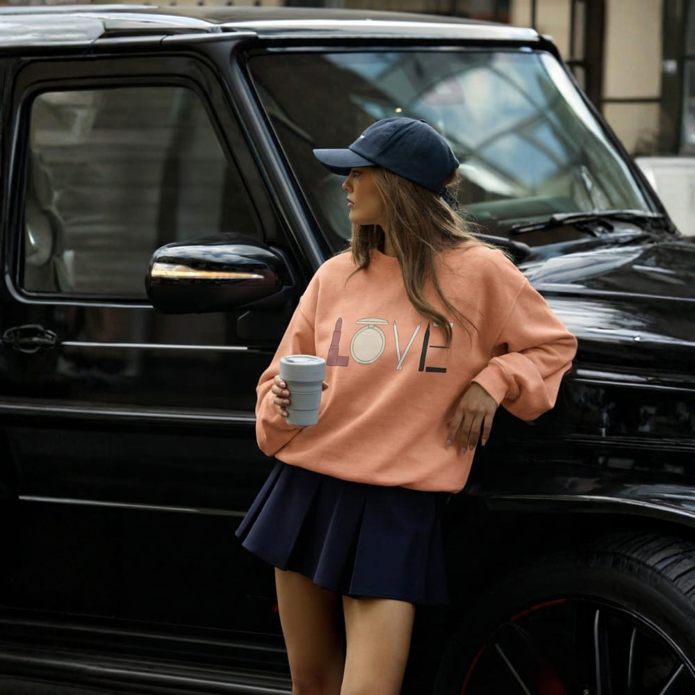 Woman in pink sweatshirt with 'LOVE' print and navy skirt standing next to a black SUV.