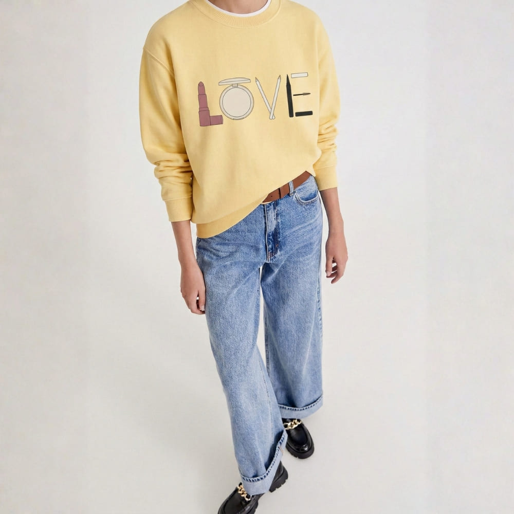 Person wearing a yellow sweatshirt with 'LOVE' printed on it and blue jeans against a white background