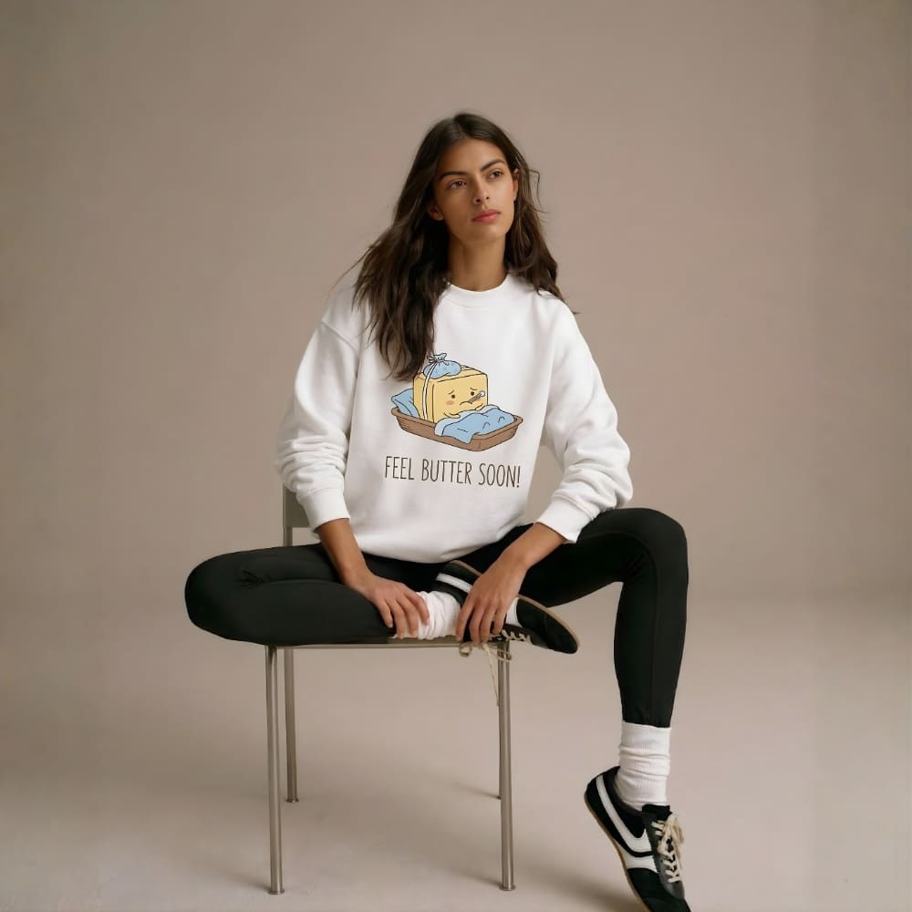 Woman wearing a white sweatshirt with a graphic design sitting on a chair against a beige background